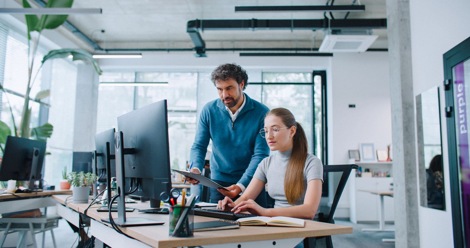 Corporate team using Ryjo products as manager compares clipboard notes with computer data while employee types and collaborates